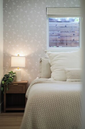 A bedroom with a bed, a nightstand, a lamp, and a window with a view of a wooden deck. - Chic 2BR on South Congress / Private Backyard (Austin)
