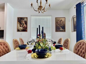 Une salle à manger avec une table blanche dressée pour six personnes, entourée de chaises rembourrées.