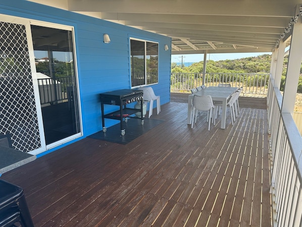 Un espacio al aire libre techado con mesa y sillas, una parrilla y un ventanal corredera.