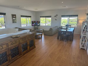 Un salón amplio con suelo de madera, una mesa de comedor con sillas, un sofá y un televisor montado en la pared.