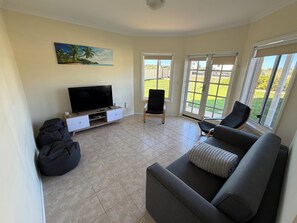 A living room with a flat-screen TV, a sofa, a chair, and a bean bag. - Sea Breeze Beach House -
 Entire home in Dongara (Dongara)