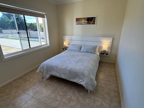 Un dormitorio con una cama, dos lámparas de noche, una ventana y un cuadro en la pared.