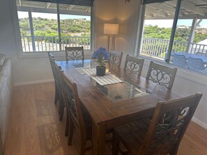 A dining area with a glass-top table, six chairs, a potted plant, and a view of greenery through large windows. - Sea Breeze Beach House -
 Entire home in Dongara (Dongara)