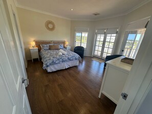 Un dormitorio con una cama grande, una silla y vistas al exterior a través de un ventanal corredera.