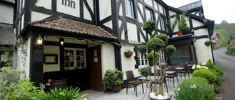 A traditional building with a sign for 'The Rock Inn' and a sign for 'Pub & Rooms'. There is outdoor seating with tables and chairs.