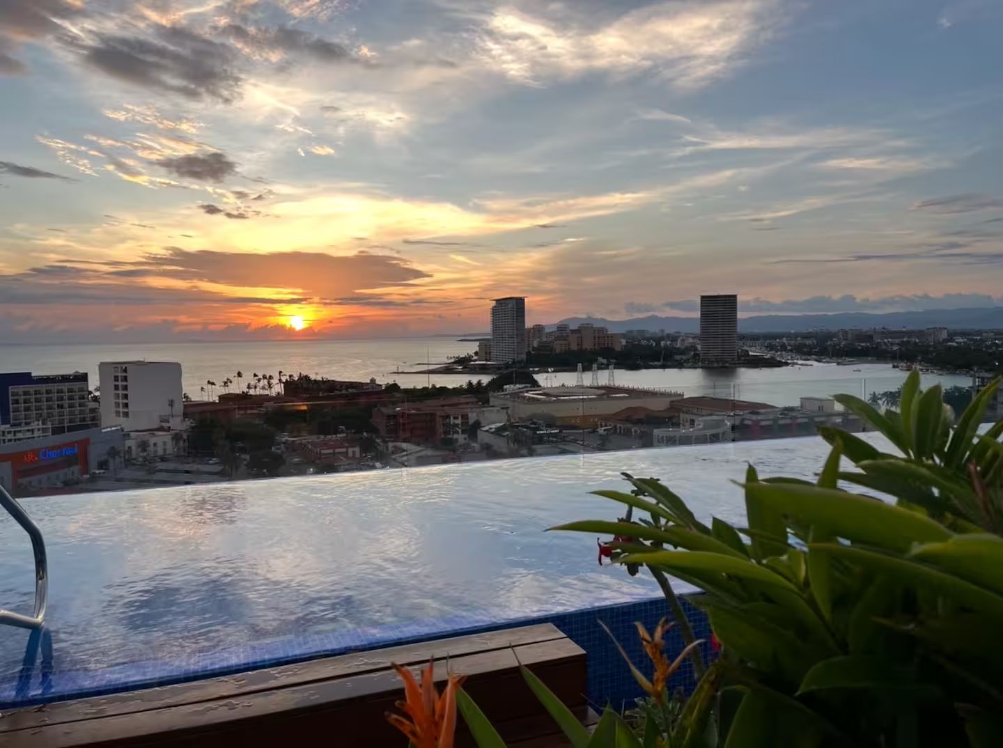 A sunset view from a balcony with a pool, overlooking a marina and cityscape.