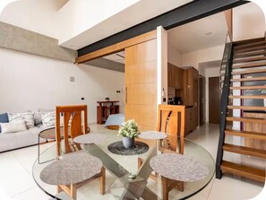 A modern living room with a glass dining table, wooden chairs, a sofa, and a staircase. - Rojo Surf Loft | beach view two story loft (Puerto Vallarta)
