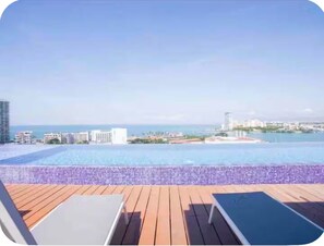 A poolside view with a clear sky, a wooden deck, and a cityscape in the background. - Rojo Surf Loft | beach view two story loft (Puerto Vallarta)