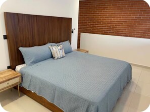 A bedroom with a bed, nightstands, a wooden headboard, a brick wall, and a tiled floor. - Rojo Surf Loft | beach view two story loft (Puerto Vallarta)