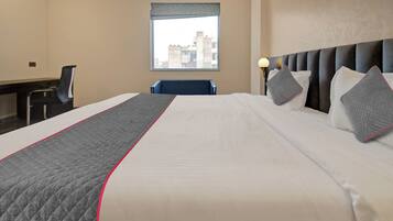 Habitación de hotel con una cama grande, un escritorio, una silla y una ventana con vista a la ciudad.