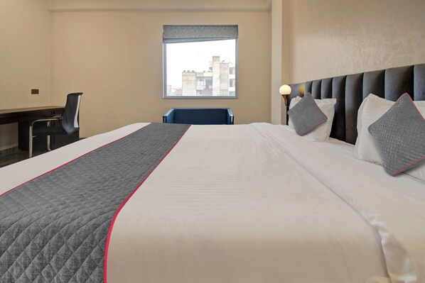 A hotel room with a large bed, a desk, a chair, and a window with a city view.