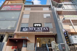 Un hotel llamado 'OYO My Stay' con una fachada moderna, varias ventanas y una entrada visible.