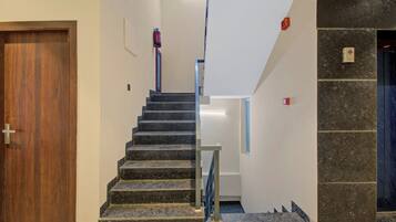Una escalera con barandilla que lleva a un piso superior, una puerta a la izquierda y un extintor colgado en la pared.
