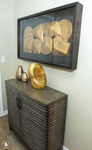 Una obra de arte abstracta enmarco sobre una consola de madera oscura con jarrones decorativos.