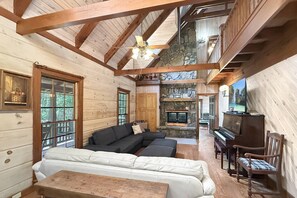 A log cabin interior with a sectional sofa, a television, and a stone fireplace. - Free Ruby Falls Ticket | Mountain View Log Cabin | Mini Golf + Fire Pit | 5 minutes Cloudland Canyon (Rising Fawn)