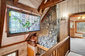 A wooden interior with a stone wall, a wooden staircase, and a stained glass window. - Free Ruby Falls Ticket | Mountain View Log Cabin | Mini Golf + Fire Pit | 5 minutes Cloudland Canyon (Rising Fawn)