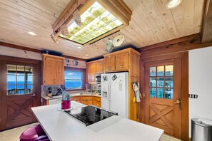 Een keuken met houten kasten, een centraal eiland met een fornuis en uitzicht door de ramen.