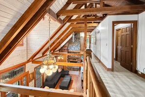 A loft-style room with a high ceiling, exposed wooden beams, a stone fireplace, and a seating area with a sofa and ottoman. - Free Ruby Falls Ticket | Mountain View Log Cabin | Mini Golf + Fire Pit | 5 minutes Cloudland Canyon (Rising Fawn)