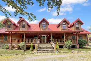 A two-story log cabin with a red roof, multiple windows, and a front porch with steps leading to the entrance. - Free Ruby Falls Ticket | Mountain View Log Cabin | Mini Golf + Fire Pit | 5 minutes Cloudland Canyon (Rising Fawn)
