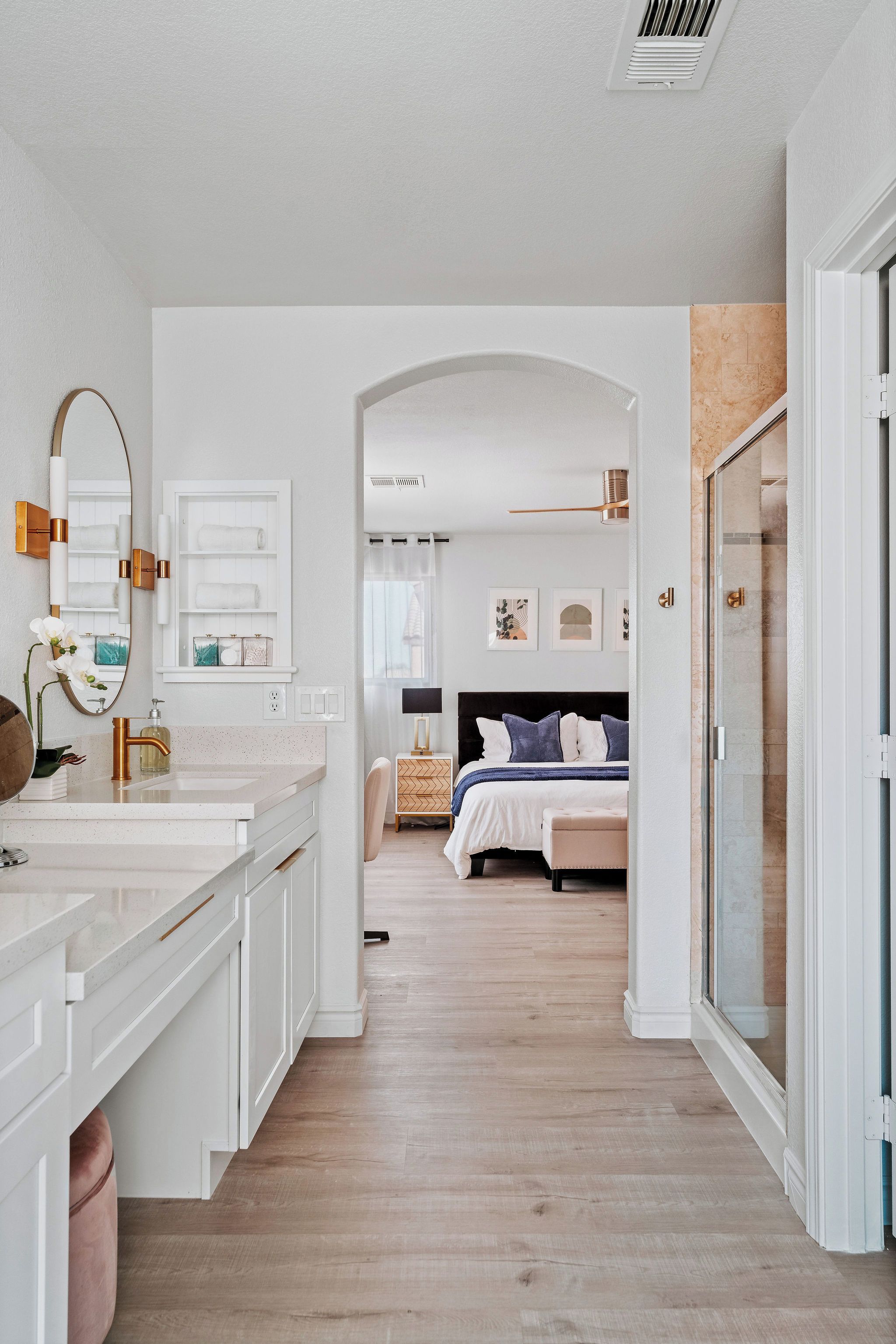 A modern bathroom with a large mirror, white cabinetry, and a vanity with a gold faucet.