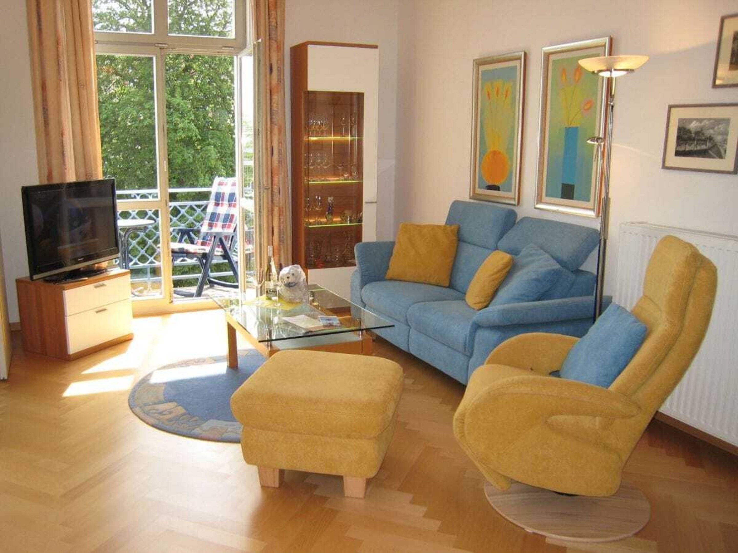 A living room with a sofa, armchair, and ottoman, a television, and a glass coffee table.