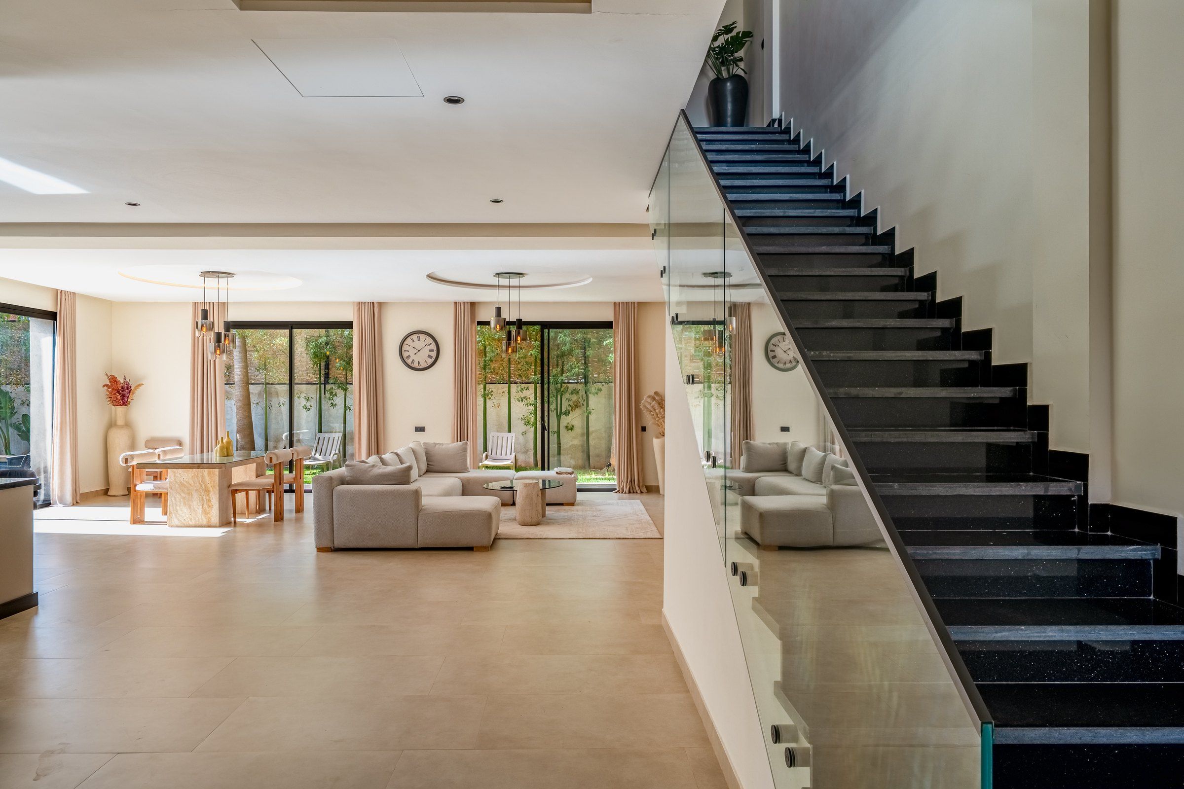 A modern living room with a staircase, large windows, and a dining area.