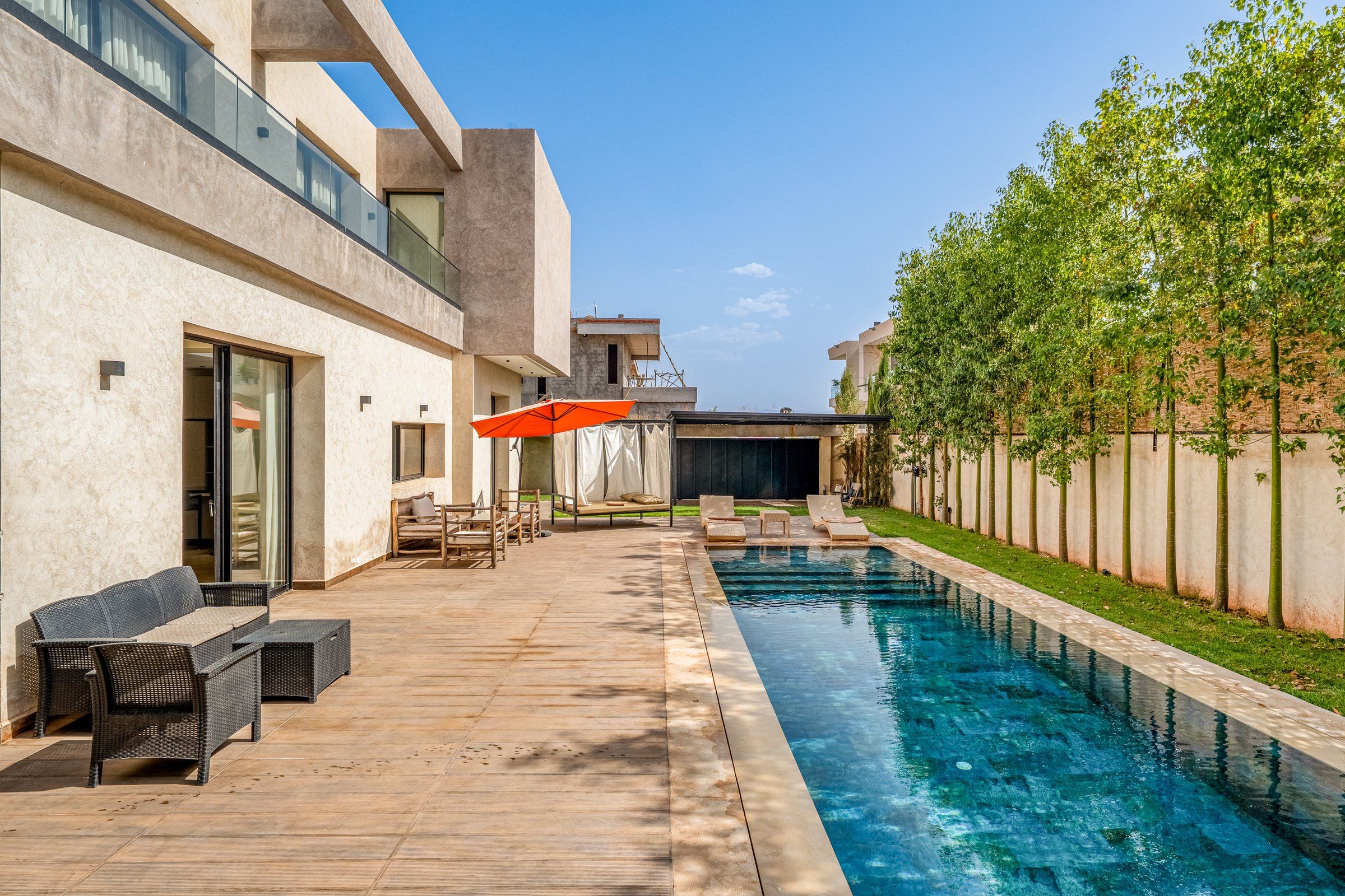 Ein moderner Poolbereich im Freien mit einer Holzterrasse, Liegestühlen und einem überdachten Sitzbereich.