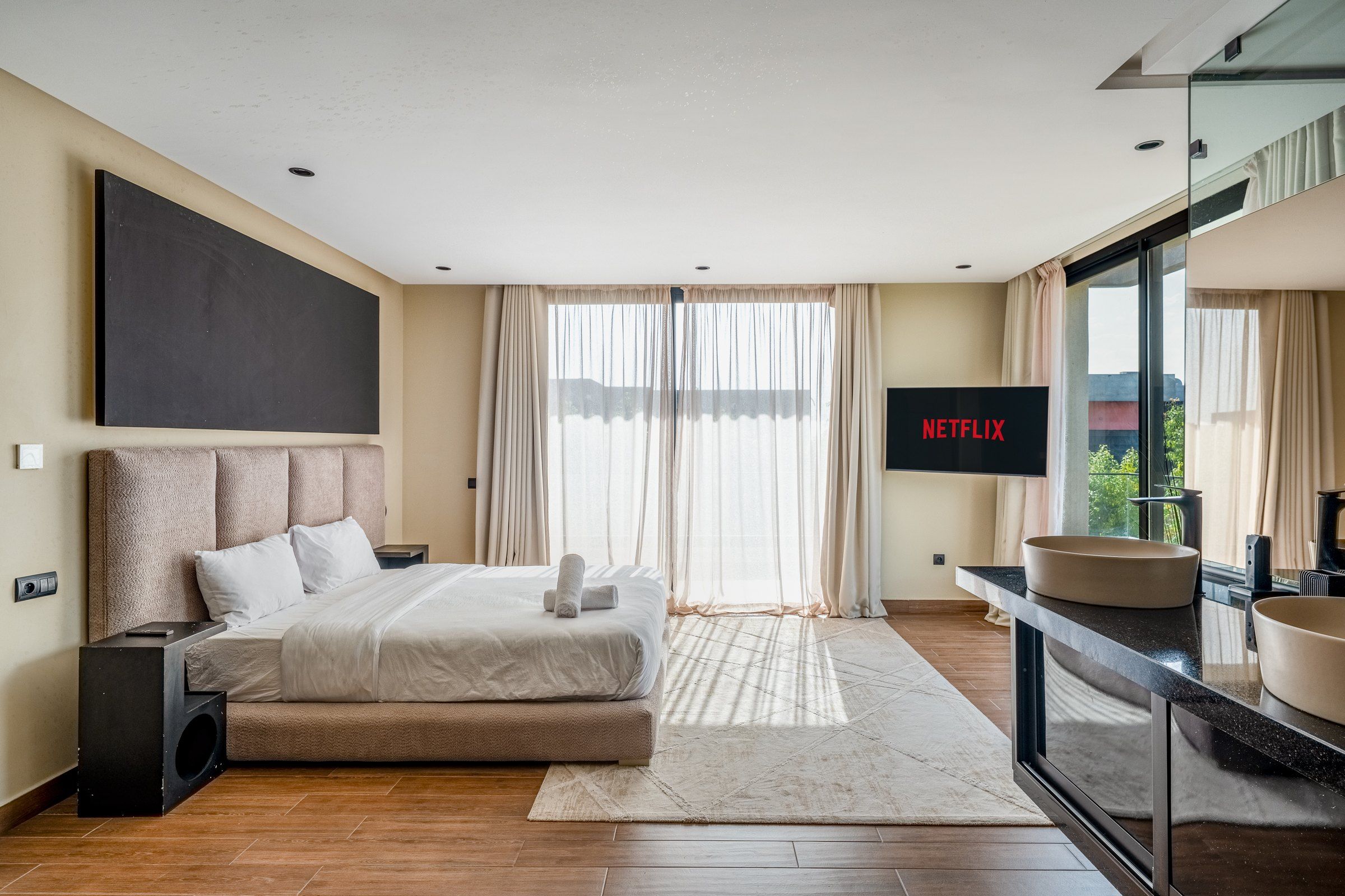 A modern bedroom with a large bed, a flat-screen TV, and a bathroom with a sink and mirror.