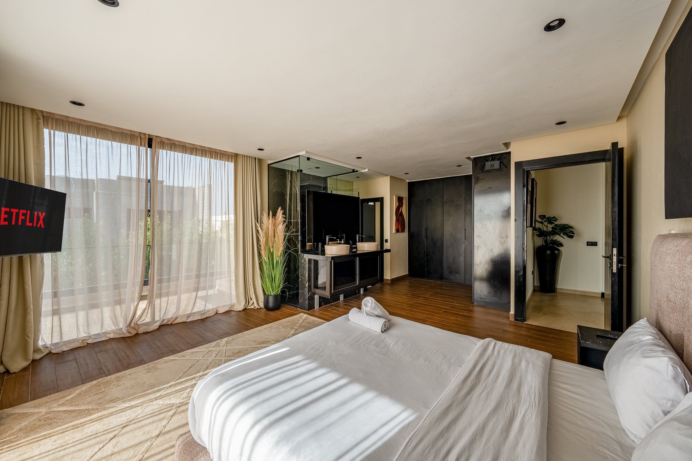 A modern hotel room with a large bed, a flat-screen TV, a bathroom with a mirror, and a view of the outdoors.