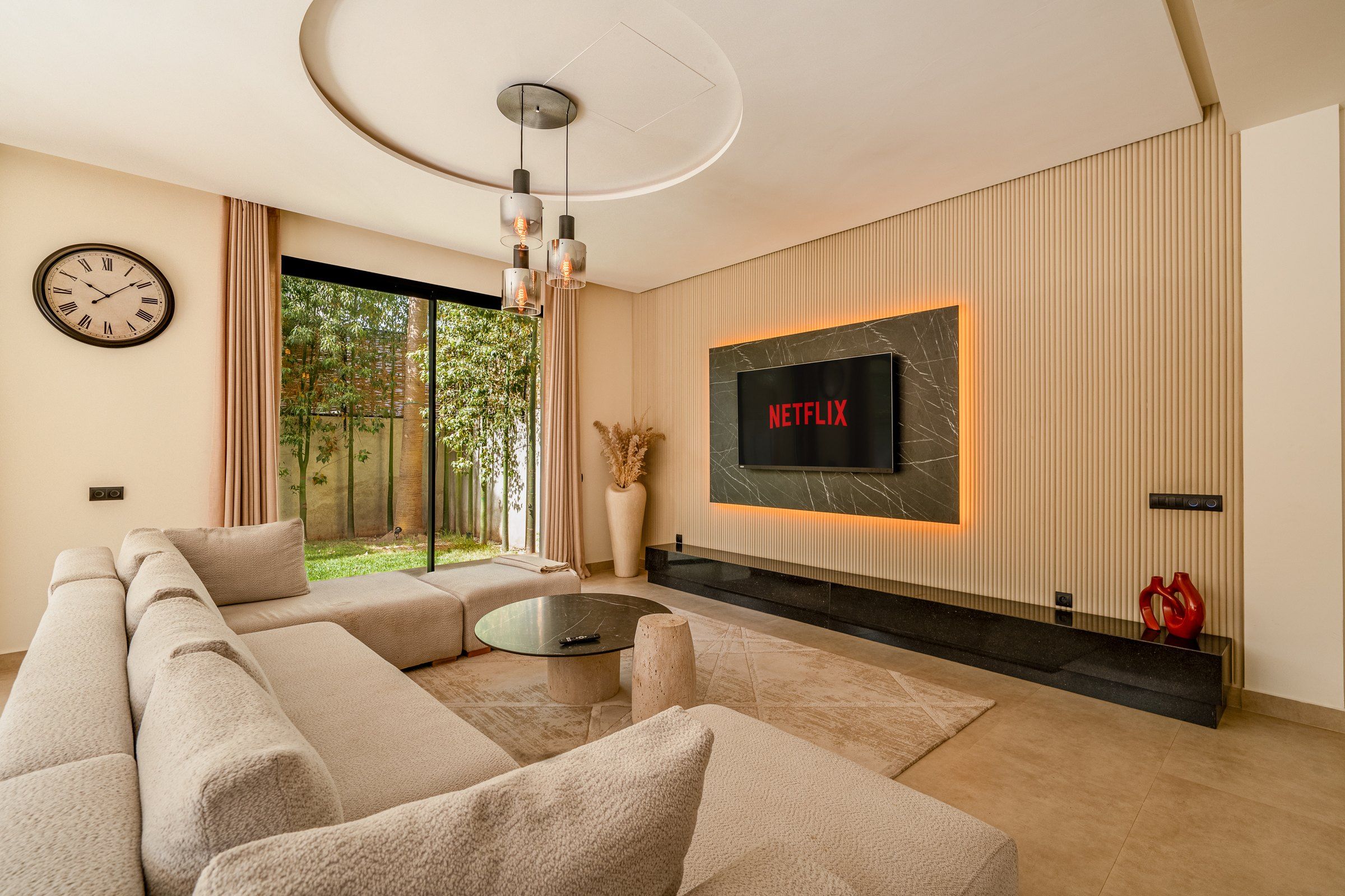A modern living room with a sectional sofa, a coffee table, a fireplace, and a large TV screen displaying 'NETFLIX'.