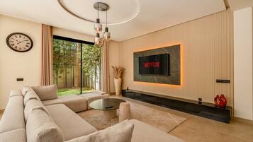 A modern living room with a sectional sofa, a coffee table, a fireplace, and a large TV screen displaying 'NETFLIX'.