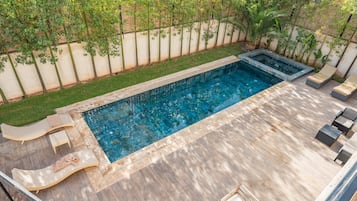 A rectangular swimming pool with a tiled deck, surrounded by a low wall and a grassy area.