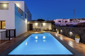 Une piscine bordée d’un muret en pierre et un espace patio aménagé avec du mobilier d’extérieur.