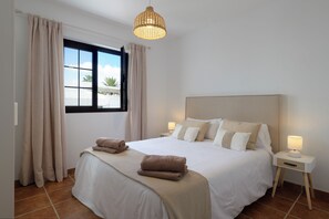A neatly made bed with a headboard, a bedside table with a lamp, and a window with curtains. - Vrbo Property (Nazaret)