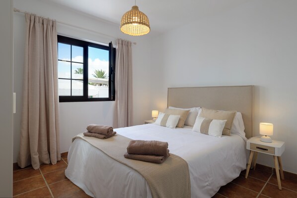 A neatly made bed with a headboard, a bedside table with a lamp, and a window with curtains. - Villa Europa: Private Pool and Space for Families and Groups (Nazaret)