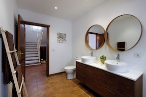 A bathroom with a double sink vanity, a toilet, a towel rack, and a door leading to a staircase. - Vrbo Property (Nazaret)