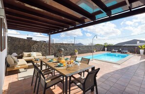 A covered outdoor dining area with a pool, stone wall, and a view of the sky and mountains. - Vrbo Property (Nazaret)