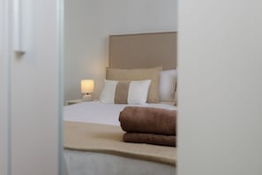 Une chambre d’hôtel avec un lit, des oreillers, une table de chevet avec une lampe et une serviette enroulée.
