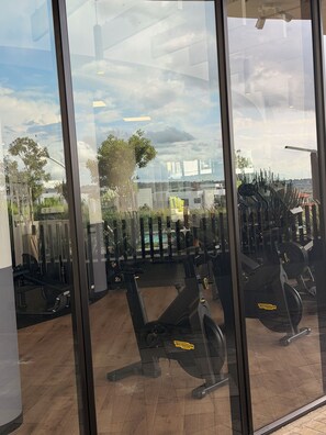 A gym with exercise equipment, a view of the outdoors through large windows, and a reflection of the sky. - Riviera Château de Rêve - Phoenix's Gîte @ Ellipse Waterfall. (Midrand)
