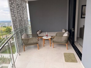A balcony with wicker furniture, a table with a bottle and glass, and a view of the cityscape. - Riviera Château de Rêve - Phoenix's Gîte @ Ellipse Waterfall. (Midrand)