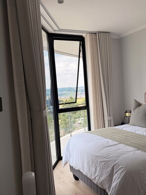 A bedroom with a large window, a bed, a bedside table, and a lamp. - Riviera Château de Rêve - Phoenix's Gîte @ Ellipse Waterfall. (Midrand)