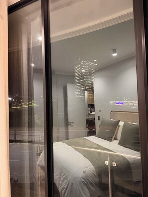A modern hotel room with a large bed, a bedside table, a mirror, and a view of the cityscape through a large window. - Riviera Château de Rêve - Phoenix's Gîte @ Ellipse Waterfall. (Midrand)