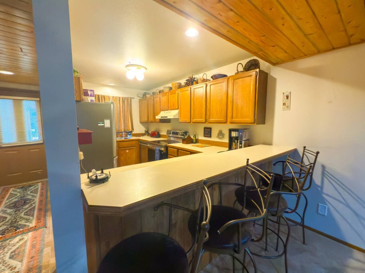 A kitchen with wooden cabinets, a bar area with metal chairs, and a built-in oven.