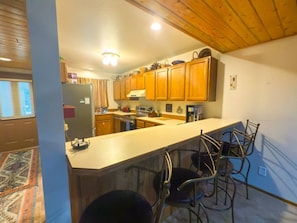 A kitchen with wooden cabinets, a bar area with metal chairs, and a built-in oven. - 3BR Big Sky Condo Sleeps 9, Walk to Free Shuttle (Big Sky)