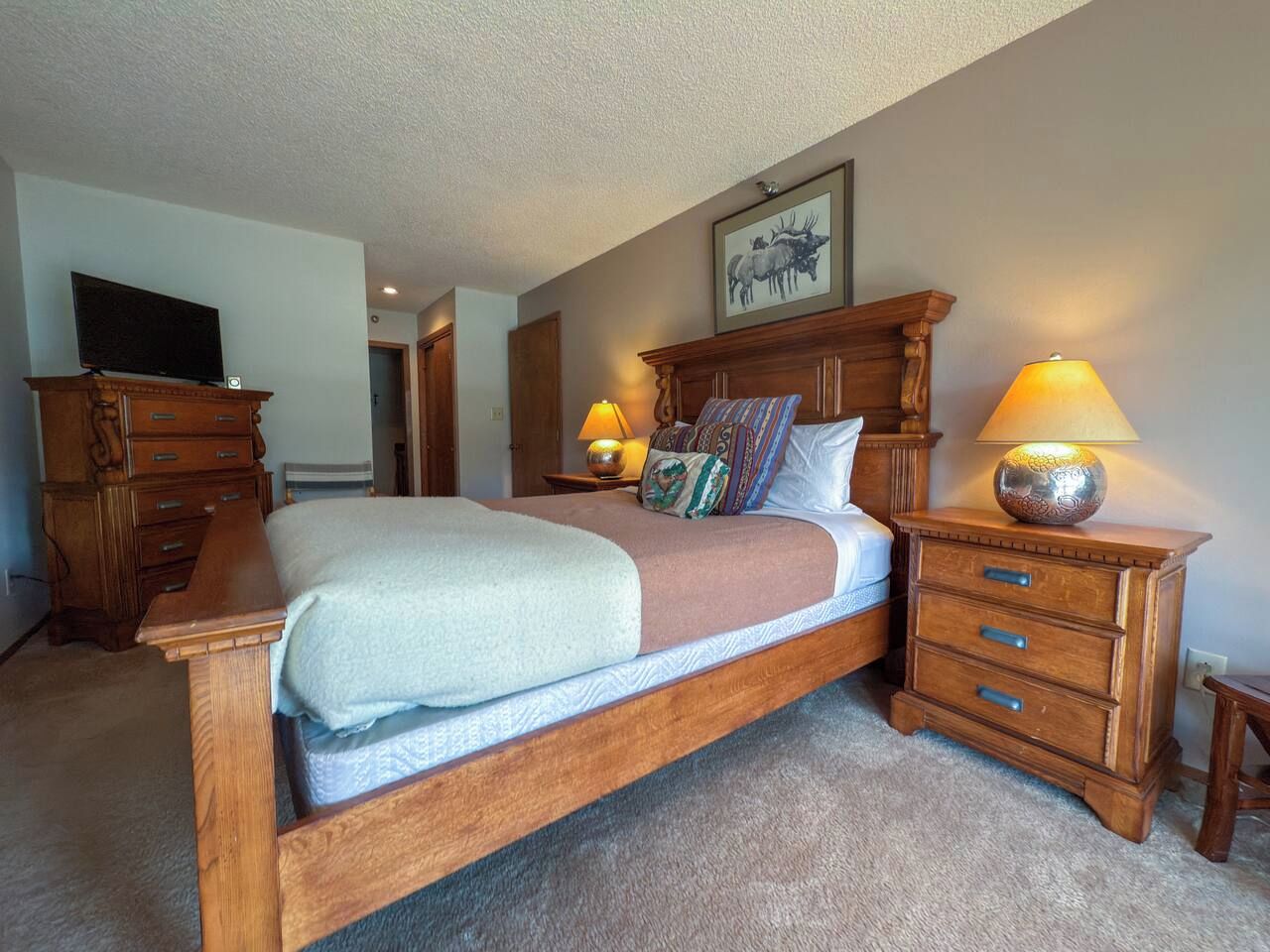 A bedroom with a wooden bed, two bedside tables with lamps, a dresser, and a television on a stand.