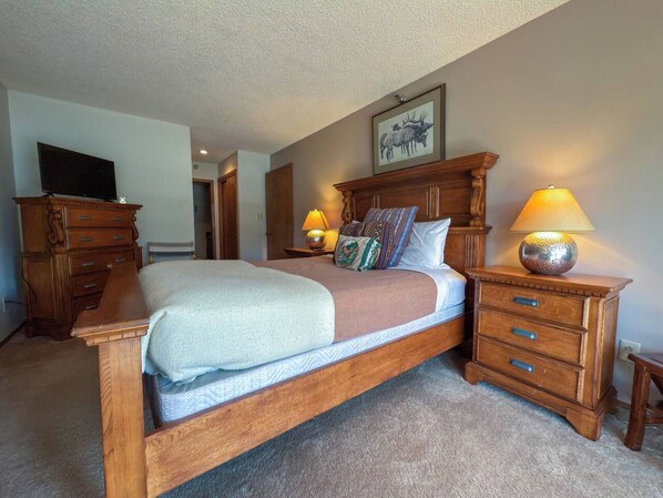 A bedroom with a wooden bed, two bedside tables with lamps, a dresser, and a television on a stand. - 3BR Big Sky Condo Sleeps 9, Walk to Free Shuttle (Big Sky)