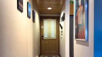 A hallway with a patterned rug, framed pictures on the walls, and a wooden ceiling.