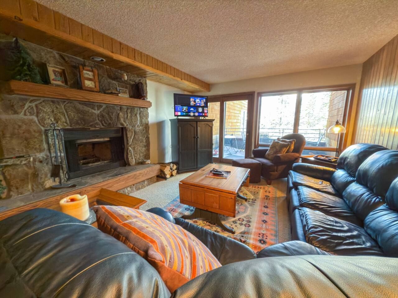 A cozy living room with a stone fireplace, leather sofa, and a television.
