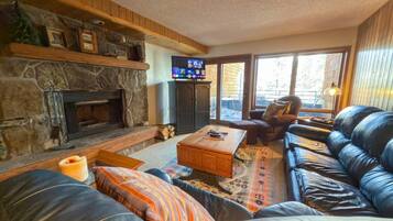 A cozy living room with a stone fireplace, leather sofa, and a television.