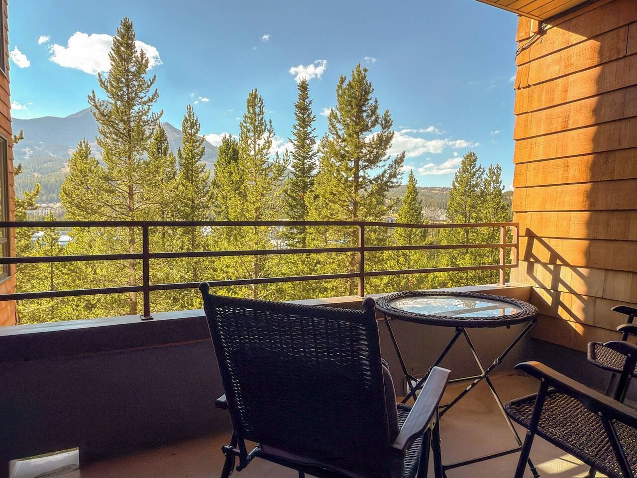 A balcony with a table and chairs, overlooking a forested mountain range.